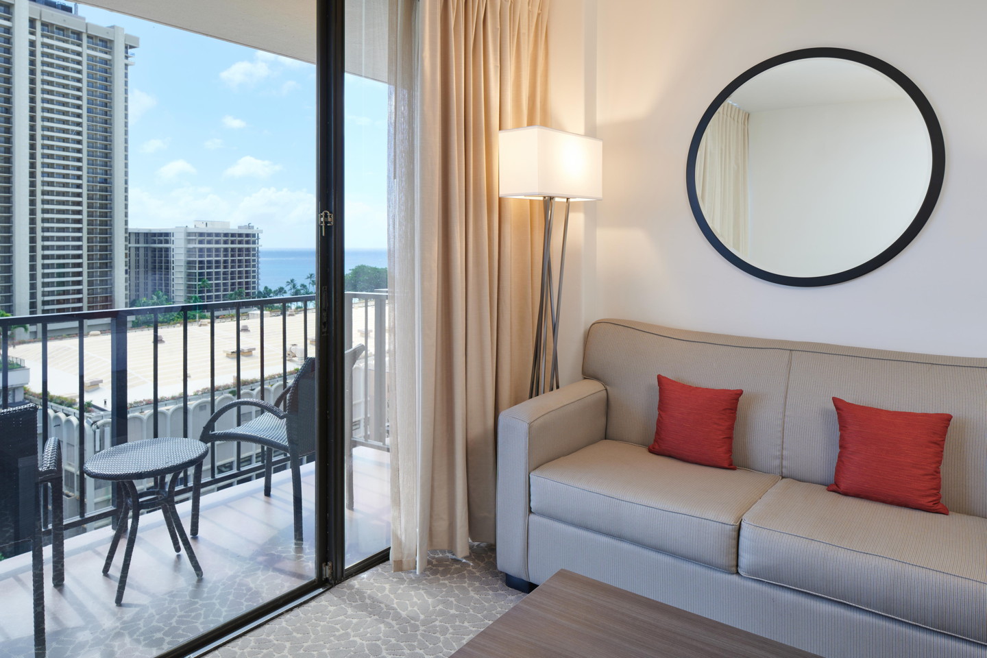 Room with couch, balcony with table and chairs, view of ocean in distance.