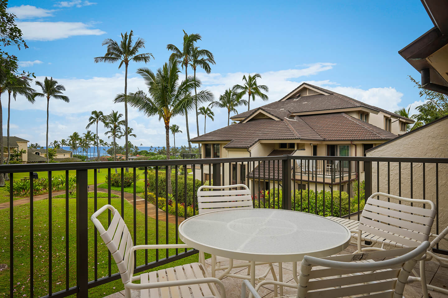 Balcony with table, chairs, and view of resort gardens and ocean.