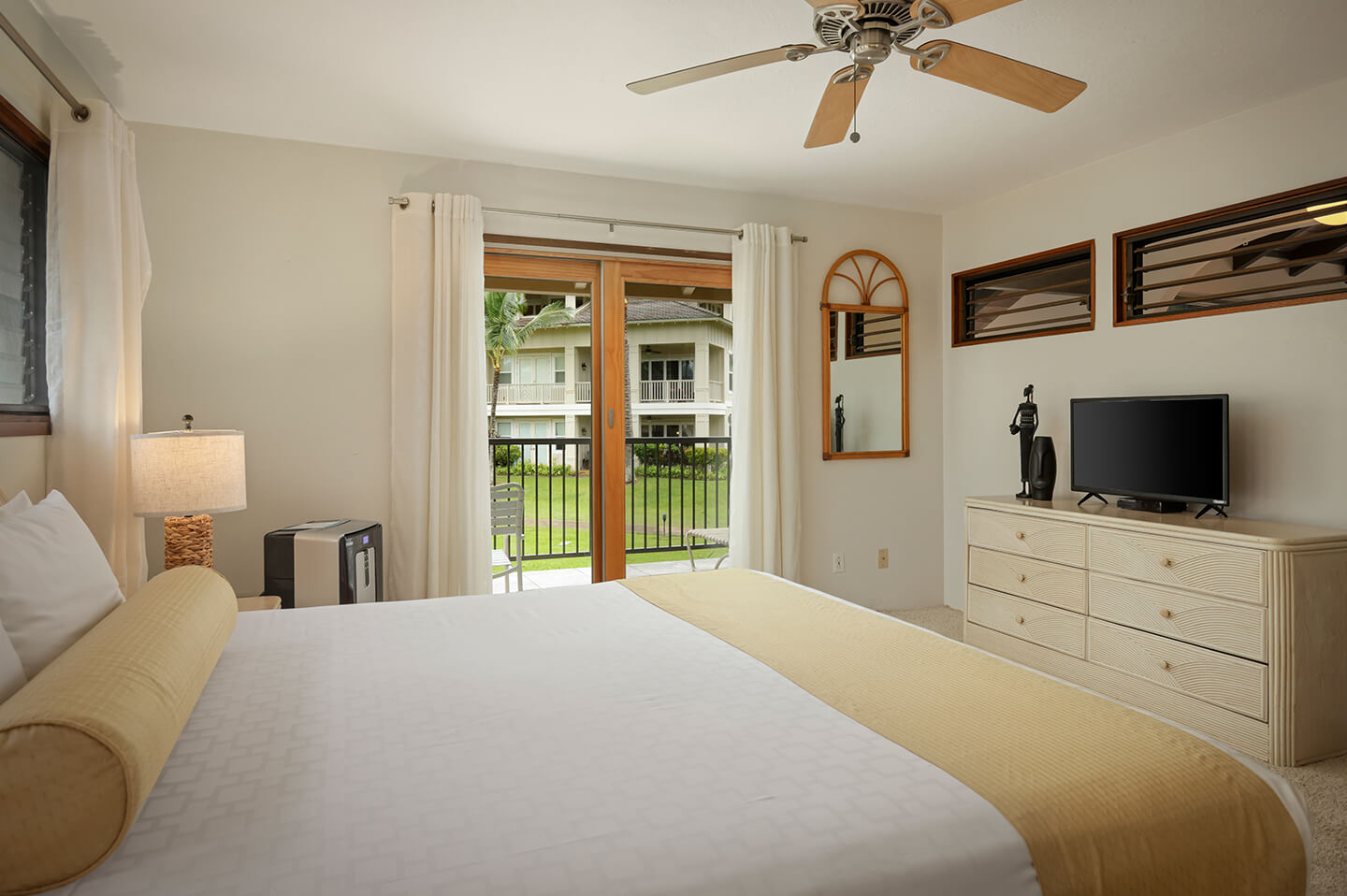 Room with bed, TV, dresser, lamp, balcony.
