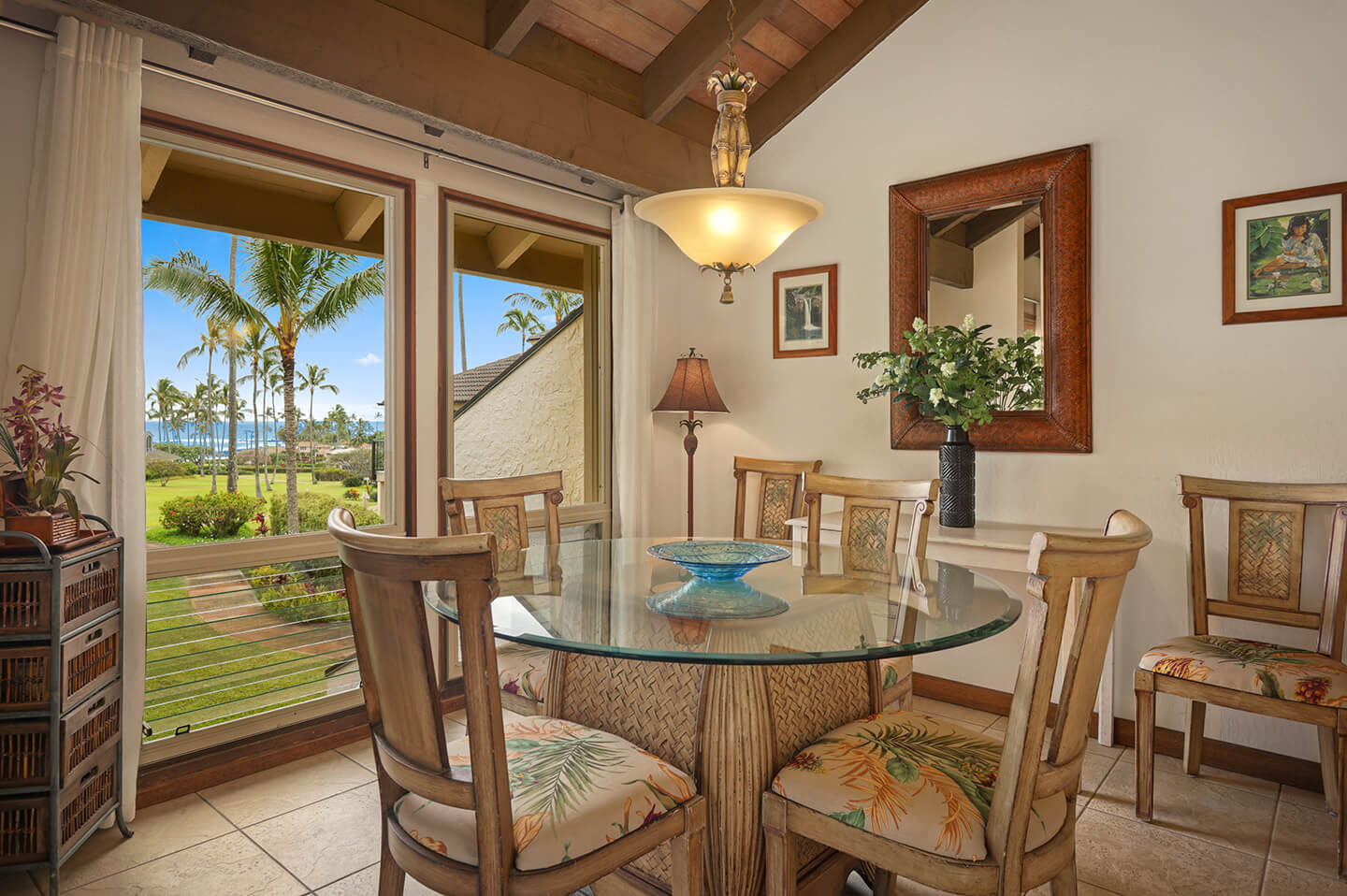Dining area with table, chairs, large windows with garden and ocean views in distance.