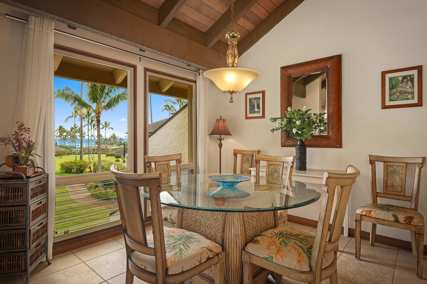 Dining area with table, chairs, and large windows with garden and ocean views in distance.