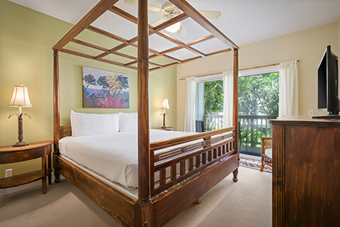 Room with 4 poster bed, night stands, lamps, TV, dresser, balcony