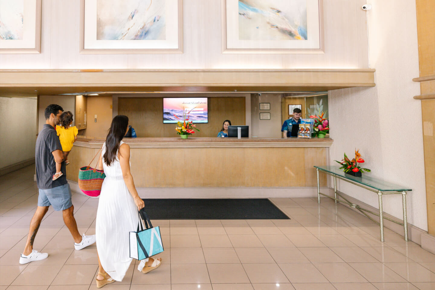 Frontdesk with husband, wife and child walking in toward front desk attendant behind the counter at Aston Waikiki Sunset