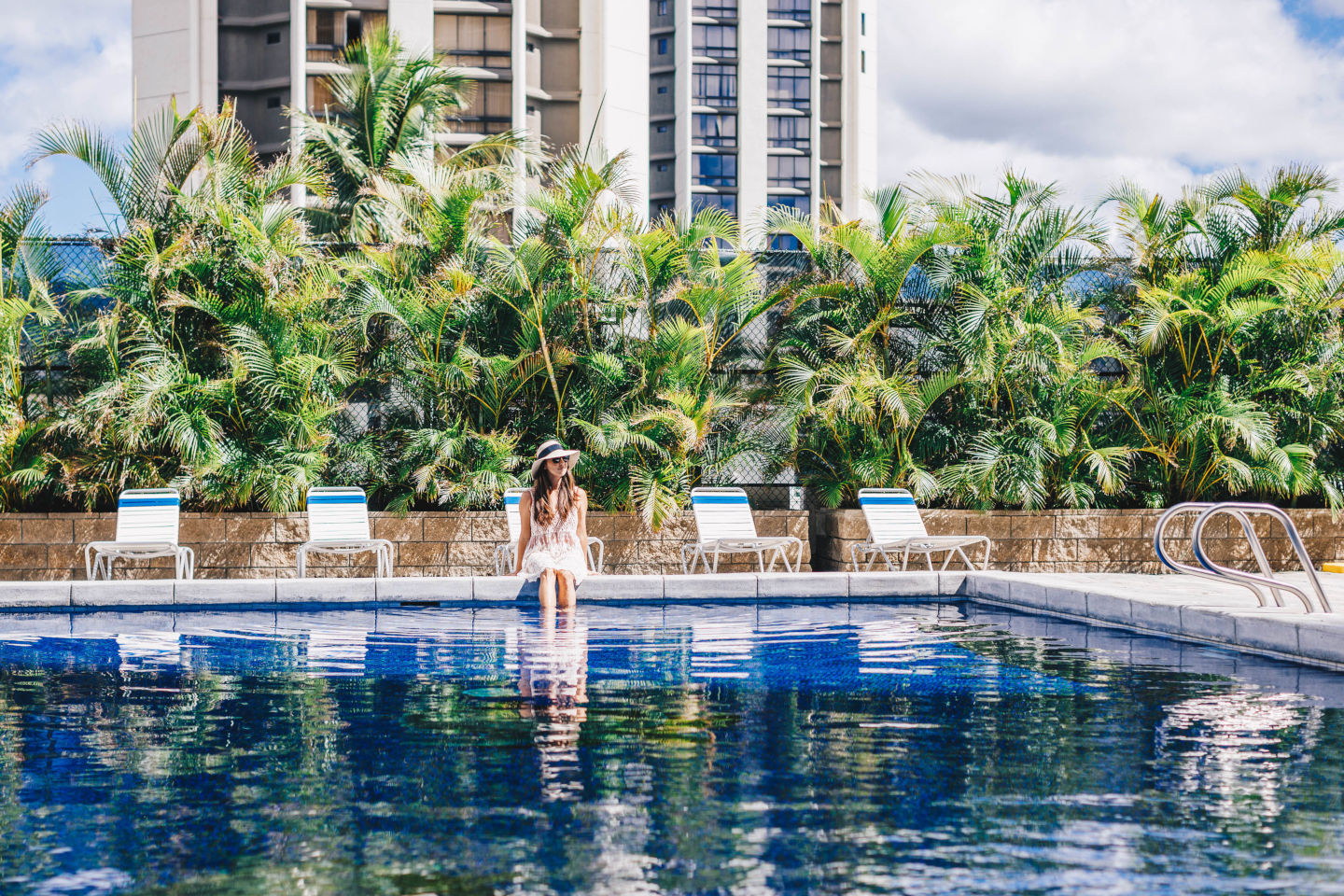 Lady with a sun hat sitting near the pool edge with her legs in the pool.