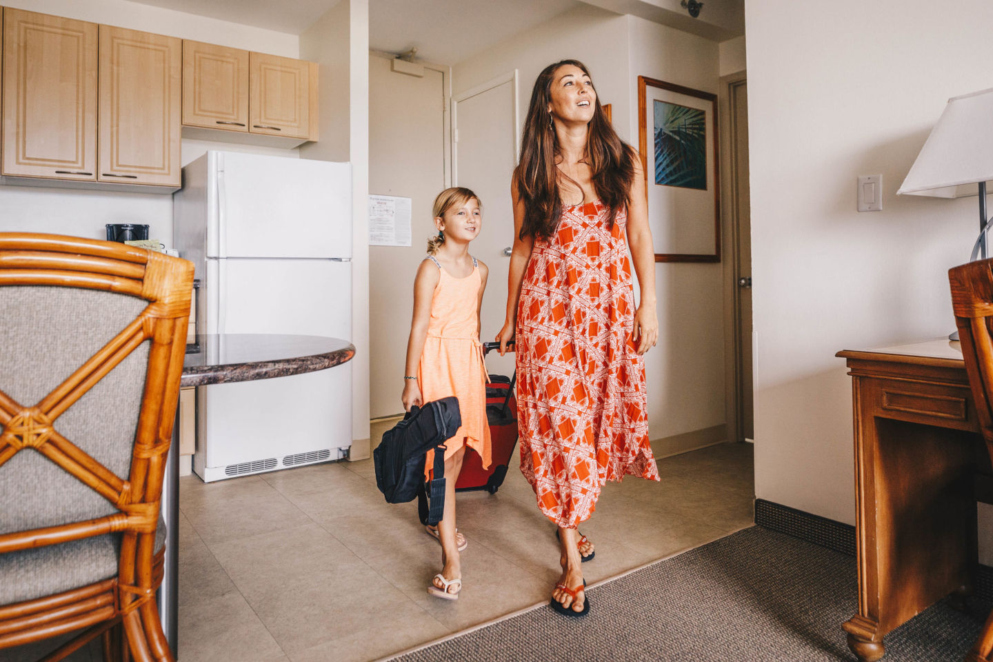 Lady and young girl are smiling as they enter the hotel room with their suitcase and bags