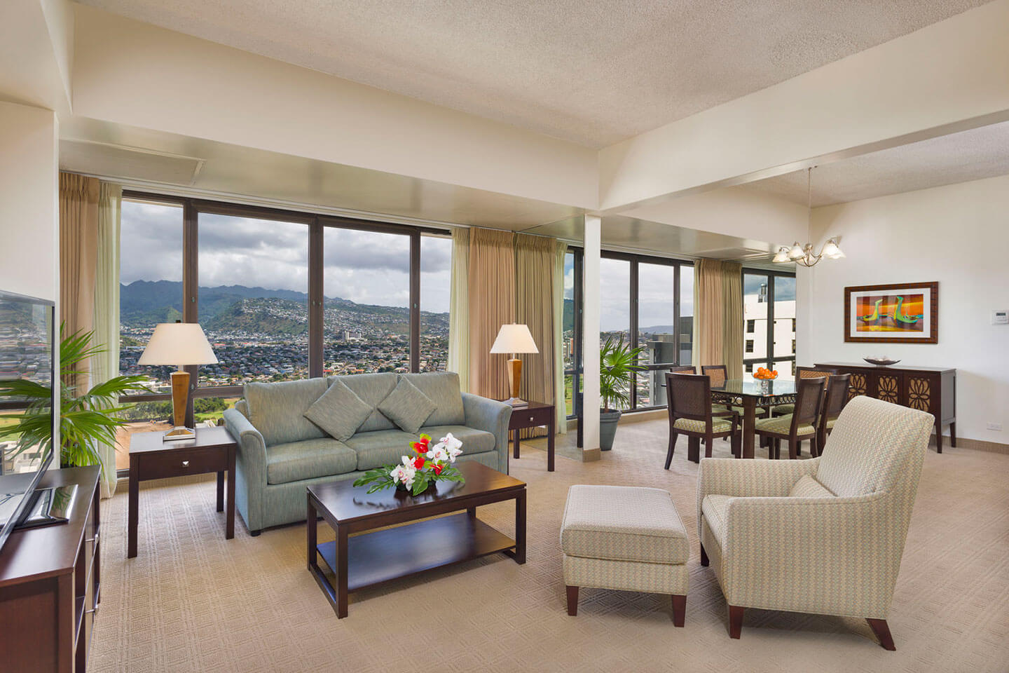 Living room with a couch, arm chair, coffee table, TV, dining area, and large picture windows with mountain views.