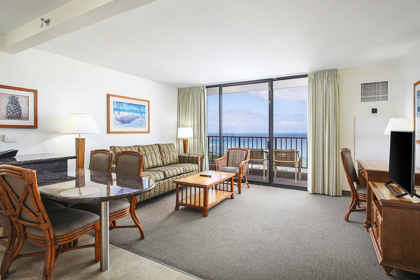 Living room with a couch, coffee table, desk, TV, dining area, and balcony with ocean view.