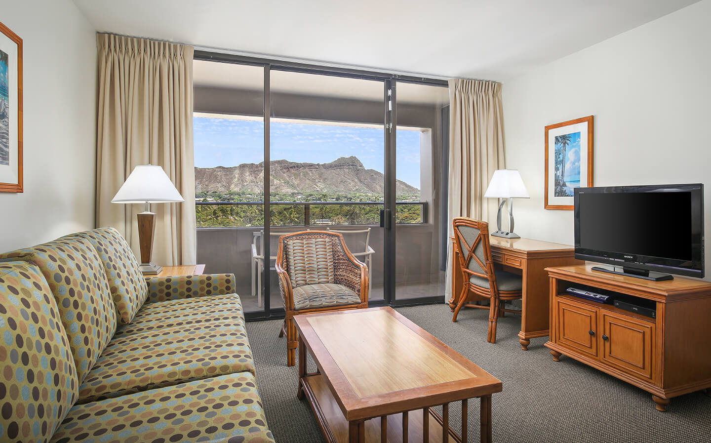 Living area with a couch, coffee table, desk, TV, and balcony with view of Diamond Head.