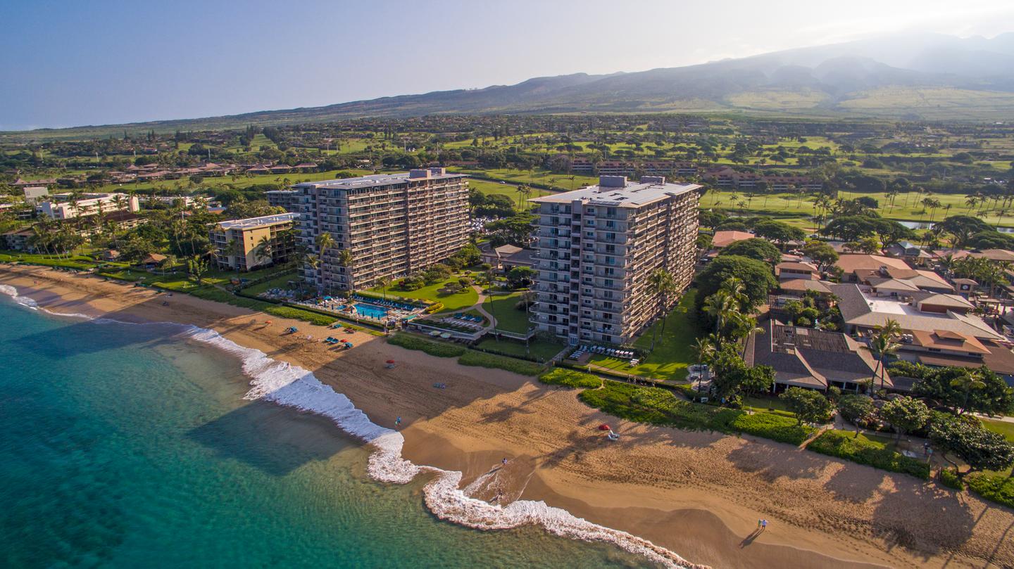 Aerial view of resort, beachfront, ocean, and mountains in the background.